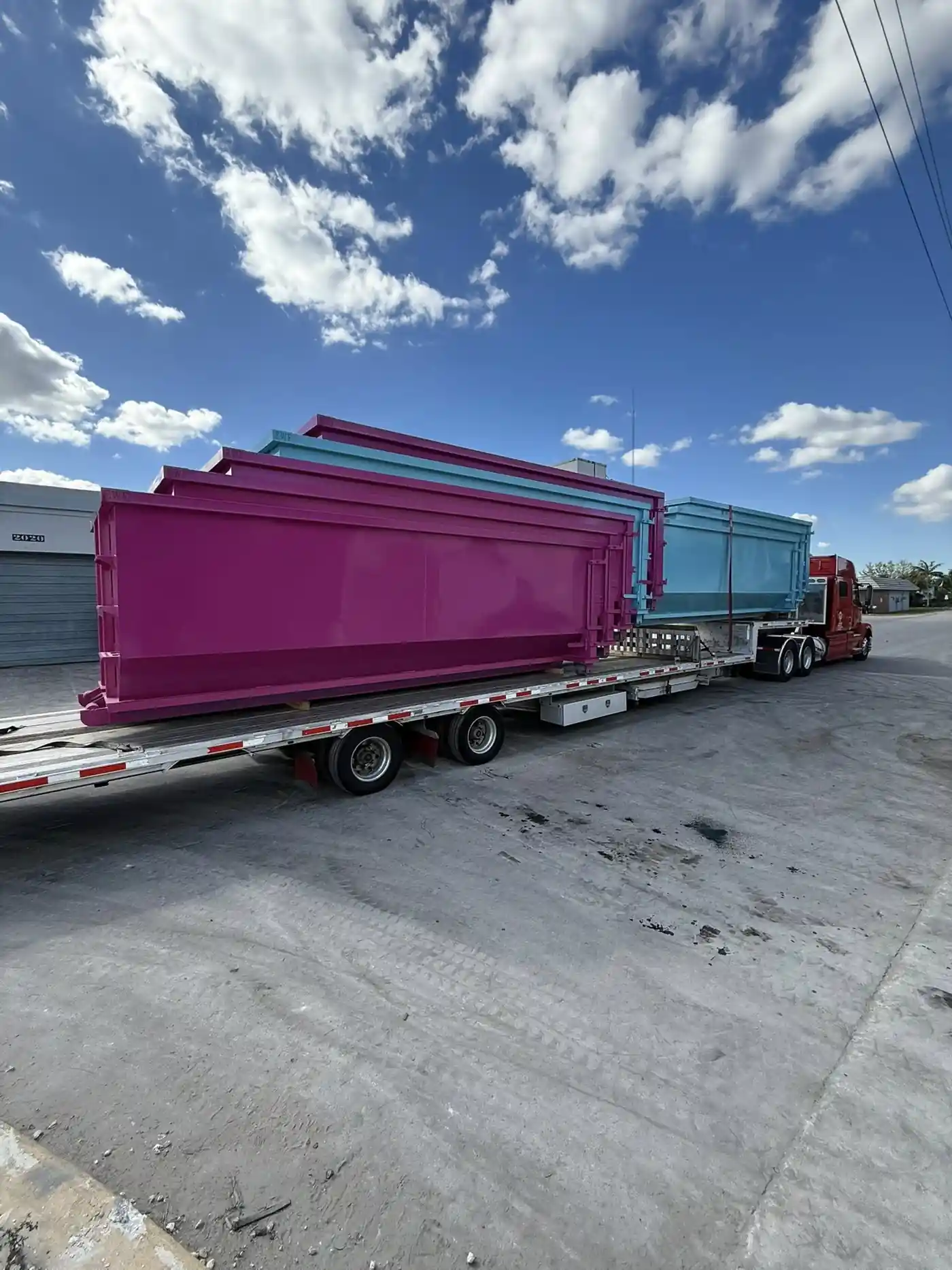 Roll off construction dumpsters being transported on a flatbed truck for delivery in Saginaw