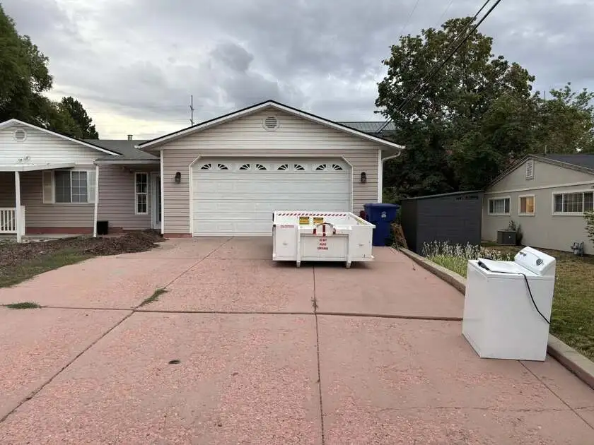 White roll-off dumpster placed on a pink concrete driveway with a discarded washing machine beside it during a home cleanout project.