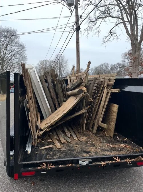 Dump trailer loaded with old wooden fencing panels, boards, and scrap lumber during a yard cleanup or demolition project.